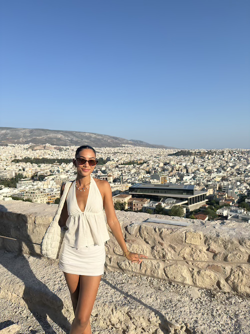 Travel creator and journalist Jenzia Burgos at the Acropolis in Athens, Greece in 2025, with panoramic views of the city below the ancient citadel.