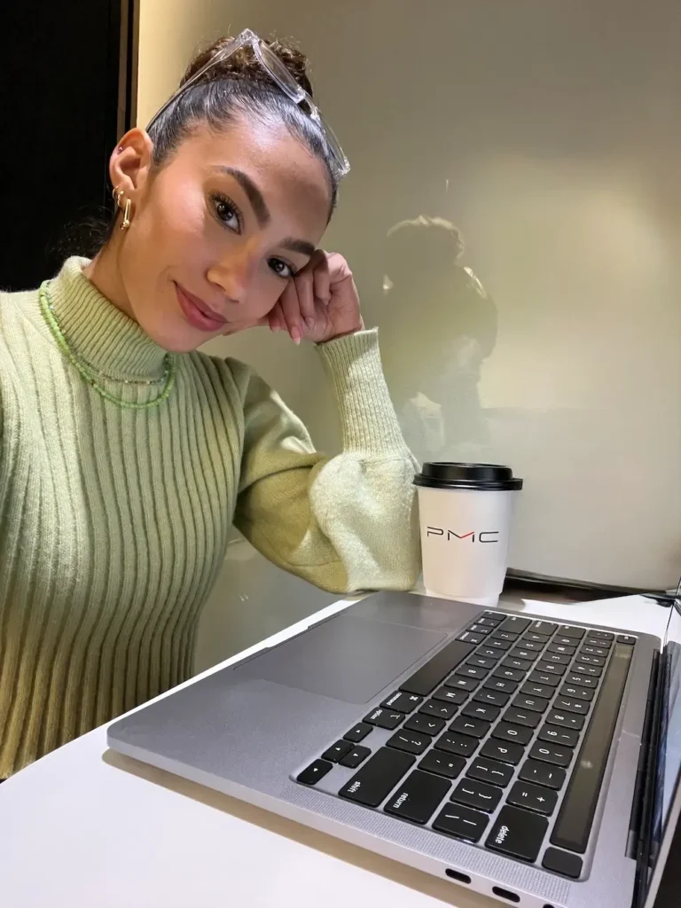 Journalist and travel creator Jenzia Burgos working from her laptop during her corporate career. She is wearing a green sweater and sitting at a desk.