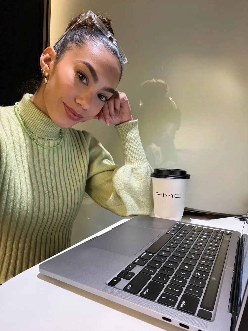 Journalist and travel creator Jenzia Burgos working from her laptop during her corporate career. She is wearing a green sweater and sitting at a desk.