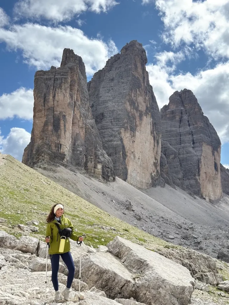 Journalist and travel creator Jenzia Burgos hiking in the Dolomites, Italy. She is holding hiking poles and wearing a lime green Patagonia jacket.