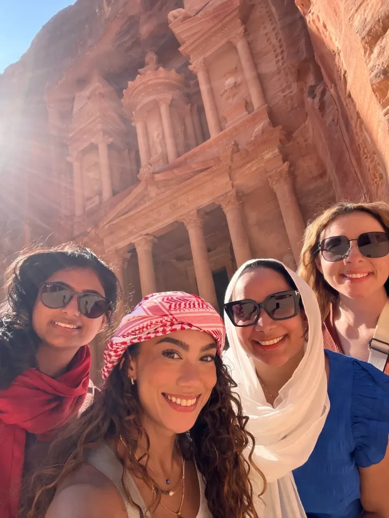 Travel blogger Jenzia Burgos and friends taking a selfie in front of Al-Khazneh (The Treasury) in Petra, Jordan, wearing traditional keffiyeh and head coverings in the ancient city.