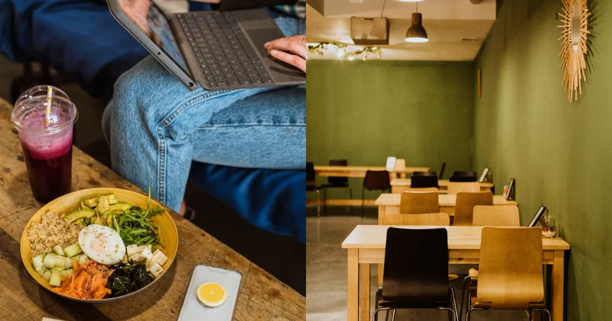 Person working on a laptop at a laptop-friendly café in Seville, Spain, with a grain bowl and berry smoothie on the wooden table; right side shows a spacious dining room with sage green walls, light wood tables, and warm pendant lighting.