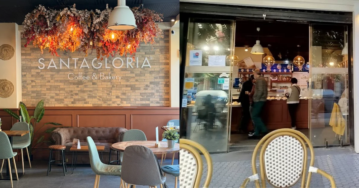 Interior of Santagloria Coffee & Bakery in Seville with a brick accent wall, a dramatic overhead floral installation with Edison bulbs, and plush seating in sage green and brown; right side shows customers at the bakery counter with bistro chairs outside.