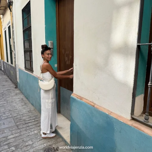 Jenzia standing in front of her teal and white apartment building entrance on a cobblestone street in Sevilla, Spain