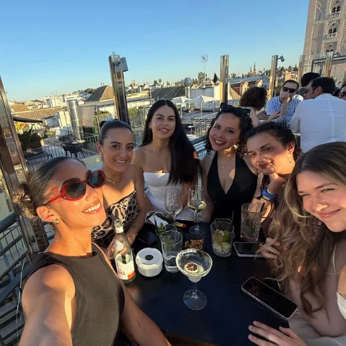 Journalist Jenzia Burgos smiling with friends at a rooftop bar overlooking Seville, Spain
