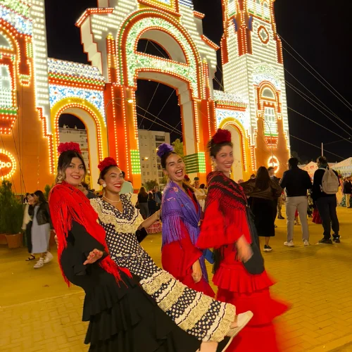 Travel writer Jenzia Burgos dressed in traditional flamenco attire at a feria celebration in Spain, with illuminated arches in the background