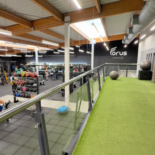 Interior of Forus gym in Seville, Spain, with weights, turf training area, and elevated track