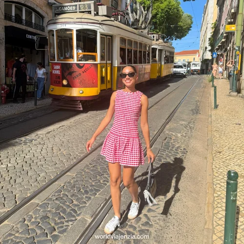 Jenzia in a pink gingham dress standing on the tram tracks in front of the iconic yellow Tram 28 in Lisbon, Portugal