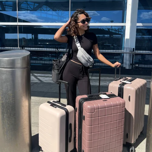 Woman with curly hair standing with mauve and beige suitcases at the airport before her flight to Spain for her English teaching program.