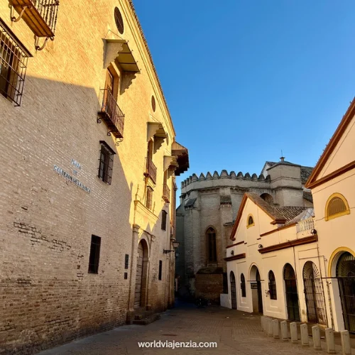 Golden-hour view of historic buildings along Plaza de Calderón de la Barca in Sevilla, Spain, with sunlit facades and a quiet cobblestone street.