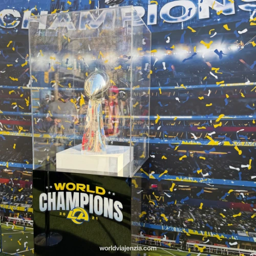 The LA Rams' Super Bowl LVI Lombardi Trophy on display in a clear case at the Melbourne fan fest, with a "World Champions 2021" sign at the base and a confetti-filled celebration backdrop.